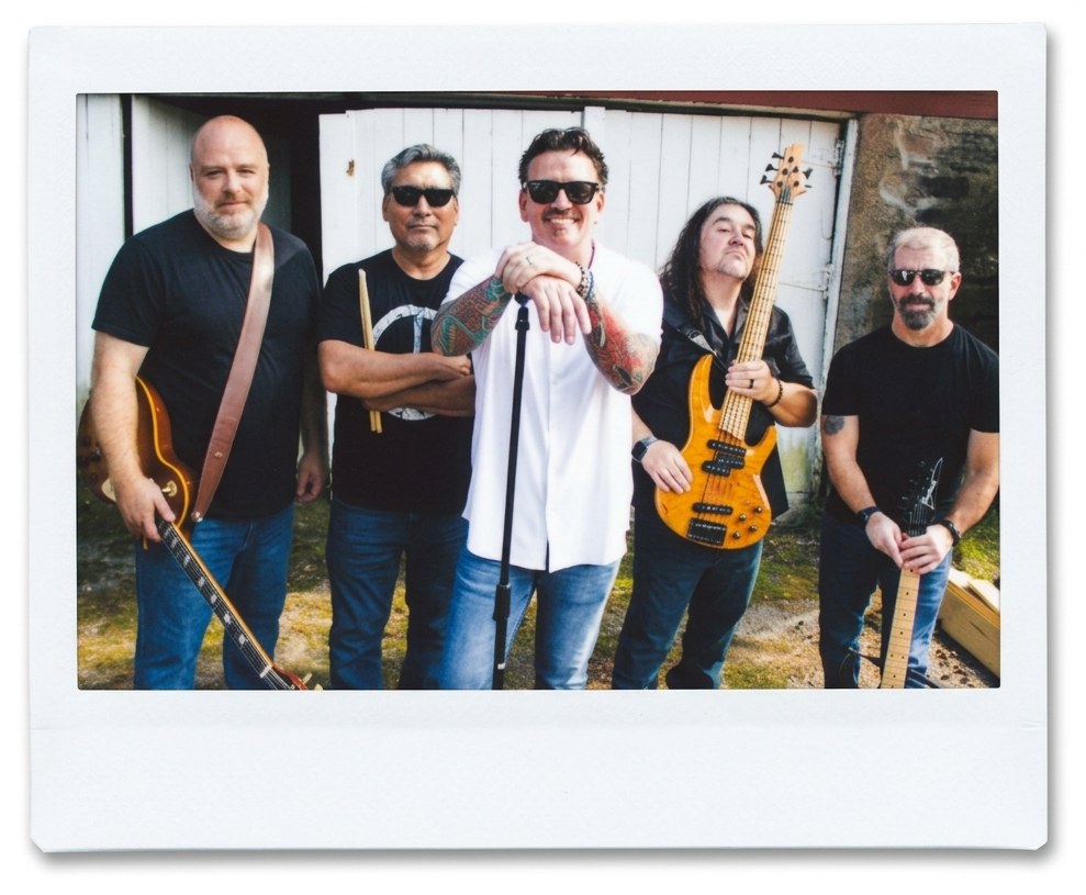 The five members of The Street Light Kids standing together outside a white barn, holding guitars, a bass and a microphone stand